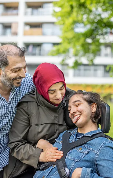 Die Eltern beugen sich beide von links zu ihrer Tochter. Die Tochter lacht. Ihre Zunge ist weit rausgestreckt. Ihre Mutter hat ihre Hand auf dem Oberkörper der Tochter. Der Vater hat seinen Arm um die Schulter seiner Frau.